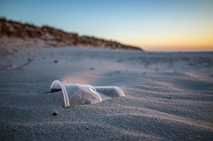 Auf dem Sandstrand gestrandeter Plastikbecher