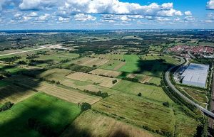Foto von norddeutscher Niedermoorlandschaft mit Feldern, Gewerbegebiet und einer Autobahnbaustelle.