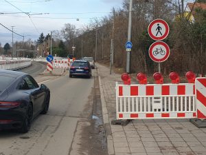 Baustellenbeschilderung: Fußgänger und Radfahrer verboten in Kombination mit Baustellenschranke auf dem Gehweg. Dahinter in detwa 15 m Entfernung ein Verkehrszeichen Radweg mit Zusatzzeichen, dass Fußgänger die Straßenseite wechseln sollen.